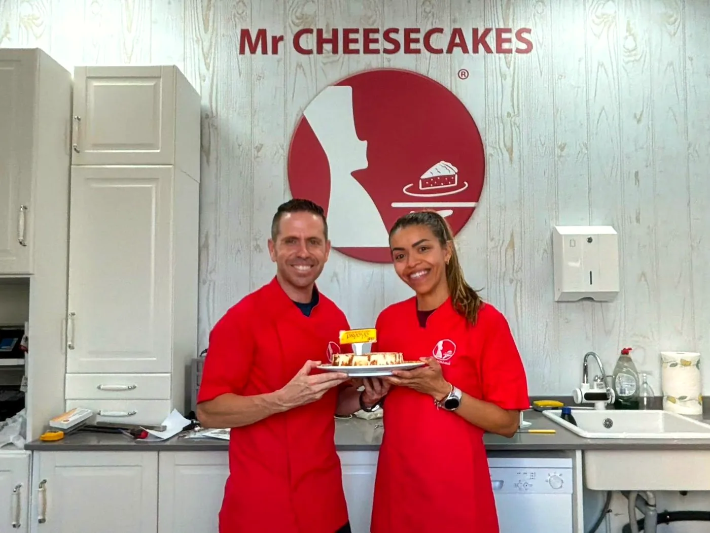 Los dos responsables de Mr Cheesecakes Sanlúcar sonriendo con una tarta de Payoyo en el obrador